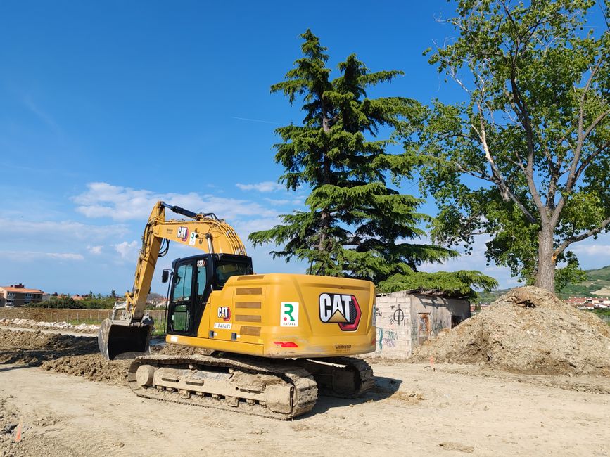 A CAT excavator working at a construction site with trees and blue sky in the background.