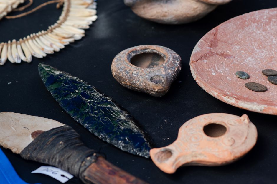 A curated display of ancient artifacts including pottery, tools, and ornaments on a black surface.