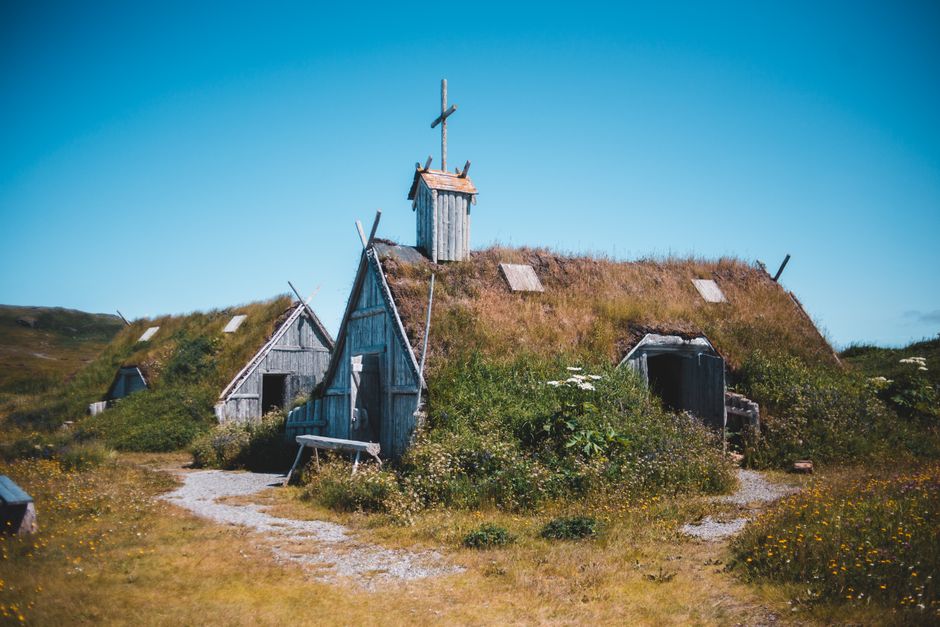Ancient wooden sod roofed church and settlement located on grassy meadow in Norstead Viking Village in Newfoundland against cloudless blue sky